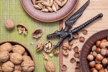 Various nuts mix in brown clay plates. Walnut, hazelnut, almond, pistachio and nutcracker on rustic background, top view, flat lay