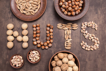 Word nuts from various type of nut. Walnut, hazelnut, almond, pistachio on brown abstract background, top view, flatlay