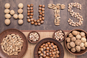 Word nuts with different type of nut. Walnut, hazelnut, almond, pistachio on brown abstract background, top view, flat lay