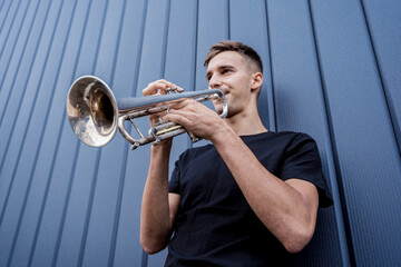 Young street musician playing the trumpet near the big blue wall