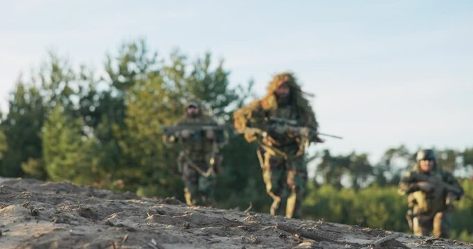 Military men in moro uniforms wearing ghillie grass moss camouflage run and lie down on ground guns on stand with scopes prepare to fire at attacker from concealment training ground