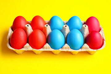 Holder with red and blue Easter eggs on color background