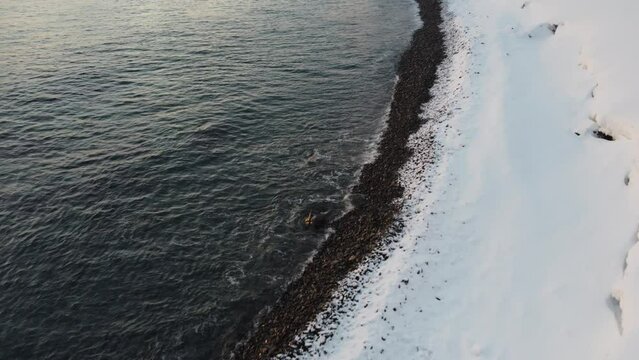 snowy pebble sea shore in winter with deep snow and cold waves