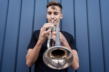 Young street musician playing the trumpet near the big blue wall