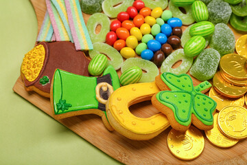 Wooden board with different sweets for St. Patrick's Day celebration on green background, closeup