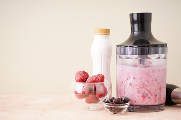 Hand blender for mixing organic fresh fruits smoothie on a color background, space for text,...