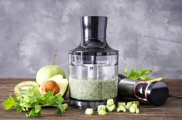 Black plastic electrical hand blender and accessories with fruit on wooden background.