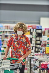 Grocery Shopping. A Guy With Face Mask Buying Food In Supermarket, Looking At Shelf With Products Walking With Shop Cart In Store.