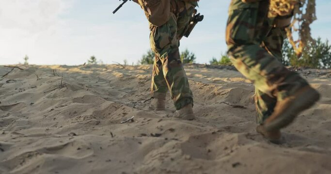 Soldiers marching on sand, field exercise, training ground, monitoring, patrolling the area, close-up of footsteps in military boots and pants, weapons in hands, troops prepared to attack