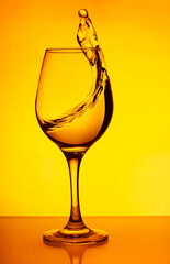 A glass of wine, a splash of wine-red water on a yellow background. A glass with a splash of wine on a yellow background. Glass on the bar in a cafe, restaurant, nightclub or disco