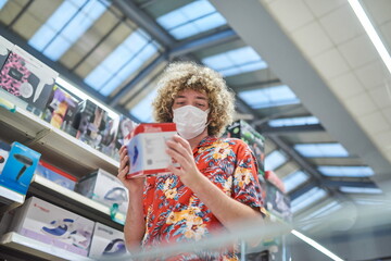 Grocery Shopping. A Guy With Face Mask Buying Food In Supermarket, Looking At Shelf With Products Walking With Shop Cart In Store.
