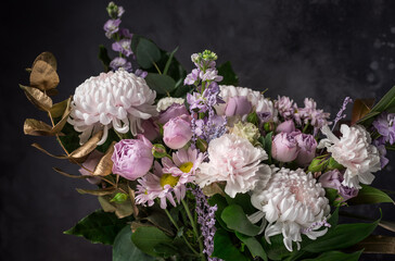 Beautiful bouquet of different flowers and golden decorative leaves on black background. Dark still life composition