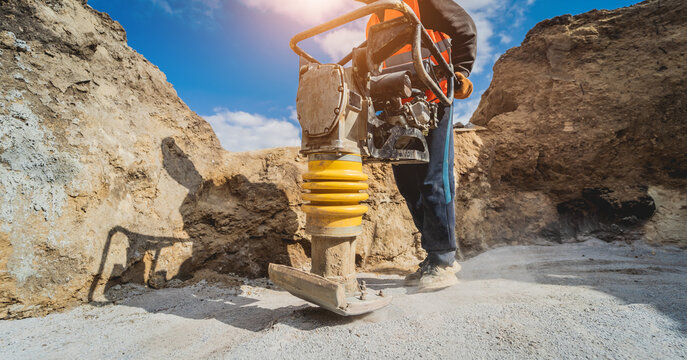 Worker uses a portable vibration rammer at construction of a power transmission substation