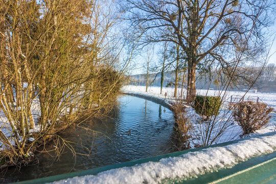 rivi&egrave;re et berges enneig&eacute;e avec arbres d'un c&ocirc;t&eacute; et pr&eacute; de l'autre et pont au premier plan