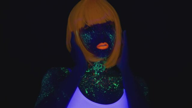 Nightclub style. Young woman with bright neon makeup wearing orange with and white t-shirt dancing in ultraviolet light
