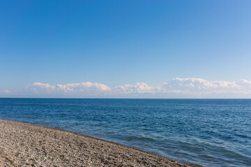 Blue calm sea and white clouds. Snow capped mountains on the horizon.