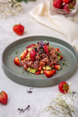 Tuna tartare with avocado and strawberries decorated with herbs and sesame seeds on light gray background. Fresh tuna tartare. European cuisine.
