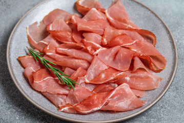 Close-up slices of prosciutto di parma or jamon serrano in a plate on gray grunge background. Side view, selective focus