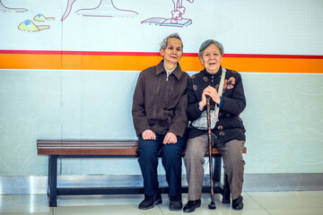 Senior Man and Woman Resting on Bench. A  senior couple, 80 years old, is sitting on a bench inside a store, relaxing. Woman holding a walking stick.