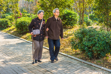 Senior Man and Woman Walking Outside. A  senior couple, 80 years old, helping each other, is walking outside, woman holding a walking stick..
