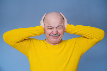 Senior man covering his ears with raised palms having terrible headache.