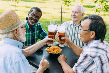 Group of senior friends drinking a beer at the park. Old multiethnic friends making activities...