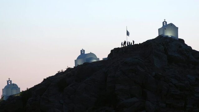 Tourists exploring the picturesque small chapels up the hill in Ios Greece while the sun is setting