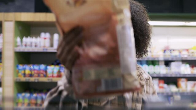 Curly woman taking corn flakes from the shelf, reads ingredients on packs
