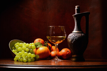 martwa natura z owocami na brązowym tle. winogron, granat, pomarańcz, czerwone róże w kompozycji z butelka wina i kieliszkiem. kompozycja na tekstura lub tapeta na pulpit. 