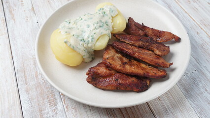 Crispy fried pork with creamy parsley sauce and boiled potato in the plate on the table or stegt flæsk, a classic Danish cuisine.