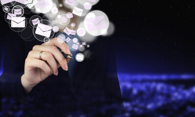 Email marketing concept. Sending newsletter. Hand holding digital graphic pen and drawing digital hologram Email and sms sign on city dark blurred background.