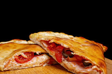 Calzone, closed pizza. Stuffing, tomatoes, bacon, cheese, olives. On a wooden board.