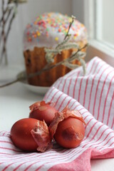 Easter eggs on a cotton napkin and Easter cake in the background. Eggs dyed with natural onions on a rustic white window background. Natural ecological coloring with food coloring. View from above.