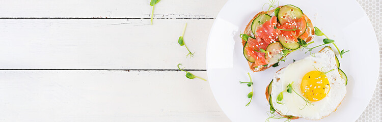 Diet breakfast. Sandwich with salt salmon salad with greens, cucumbers, fried egg and microgreen.  Top view, banner