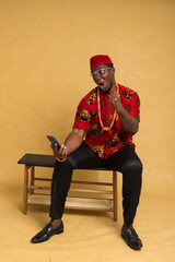 Igbo Traditionally Dressed Business Man Sitting Down and Staring at Phone and Happy