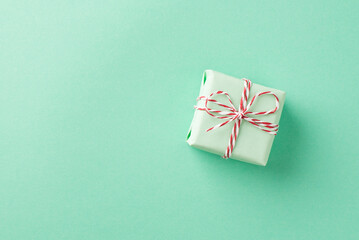 Top view photo of the small green gift box tied up with red and white cord on the pastel turquoise isolated background copyspace