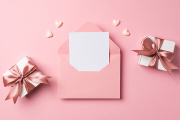 Top view photo of valentine's day decorations open pink envelope with paper sheet two small white gift boxes with pink bows and hearts on isolated pastel pink background with empty space