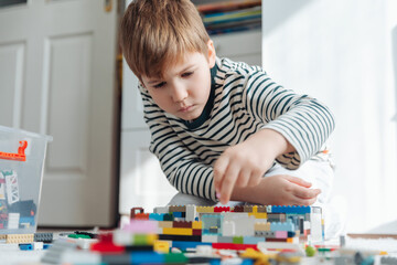 Little boy playing with construction toy blocks building a house in a sunny play room. Child and toys.