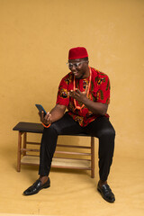 Igbo Traditionally Dressed Business Man Sitting Down and Staring at Phone and Celebrating