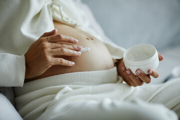 Close-up of pregnant woman applying skincare cream on her belly to prevent stretch mark