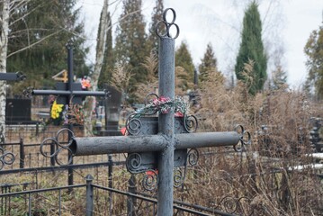 one old gray metal cross on a grave in dry grass in a cemetery
