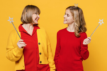 Woman 50s in red shirt crown with teenager girl 12-13 years old. Grandmother granddaughter hold magic wand fairy stick look to each other isolated on plain yellow background. Family lifestyle concept.