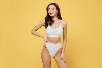 Minded beautiful lovely attractive young brunette caucasian woman 20s wear white underwear with perfect fit body standing posing look aside isolated on plain yellow color background studio portrait
