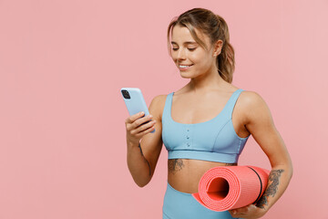 Young cool strong sporty athletic fitness trainer instructor woman wear blue tracksuit spend time in home gym hold use mobile cell phone isolated on pastel plain pink background Workout sport concept
