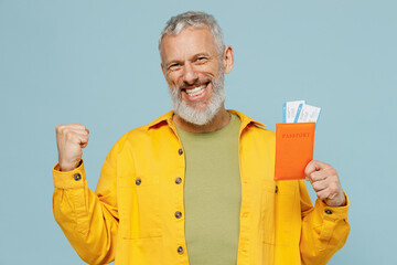 Traveler tourist elderly gray-haired bearded man in shirt hold passport ticket do winner gesture isolated on plain blue background Passenger travel abroad weekends getaway. Air flight journey concept