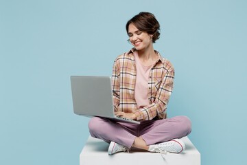 Full body young smiling copywriter happy cool woman 20s in brown shirt sit on white chair hold use work on laptop pc computer isolated on pastel plain light blue b ackground People lifestyle concept