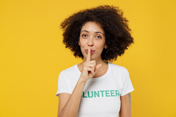Young woman of African American ethnicity in white volunteer t-shirt say hush be quiet with finger...