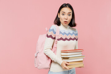Shocked scared sad teen student girl of Asian ethnicity wearing sweater backpack hold pile of books look camera isolated on pastel plain light pink background Education in university college concept.