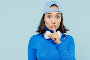 Secret young woman of Asian ethnicity 20s wears blue shirt cap headphones around neck say hush be...