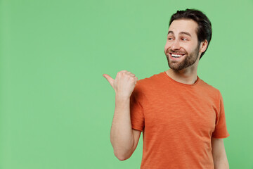 Young smiling fun man 20s wear casual orange t-shirt point thumb finger aside on workspace area...